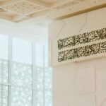 تصميم داخلي نيو إسلامي معاصر يبرز واجهة زجاجية بمشربية هندسية مفرغة وسقفاً كاسيت معالجاً مع خط عربي بارز على جدار نقي.