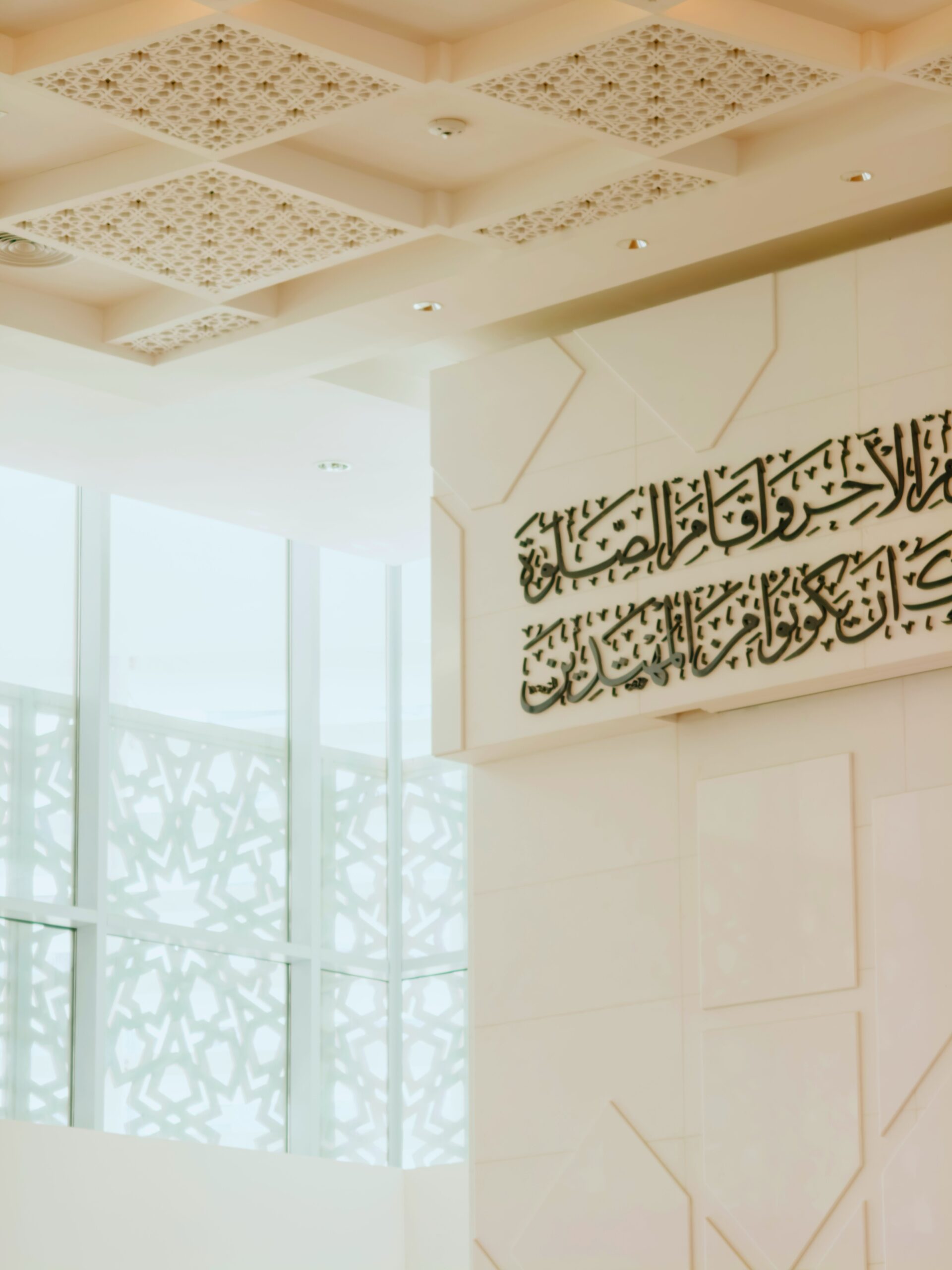 تصميم داخلي نيو إسلامي معاصر يبرز واجهة زجاجية بمشربية هندسية مفرغة وسقفاً كاسيت معالجاً مع خط عربي بارز على جدار نقي.