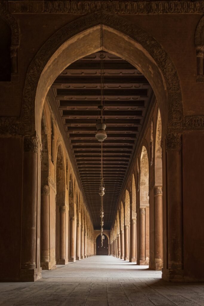 منظور داخلي لرواق مسجد أثري يجسد مصطلحات العمارة القديمة من خلال تكرار الأقواس الحجرية والأسقف الخشبية المزخرفة